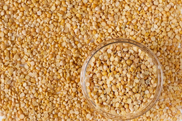 Bowl of yellow dry split peas on dry split peas background.