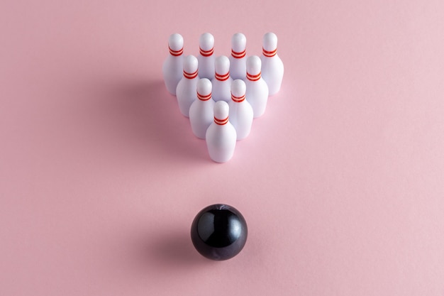 Bowling ball and white skittles on pastel pink background.