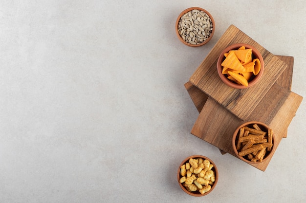 Bowls of chips, crackers and sunflower seeds on stone surface.