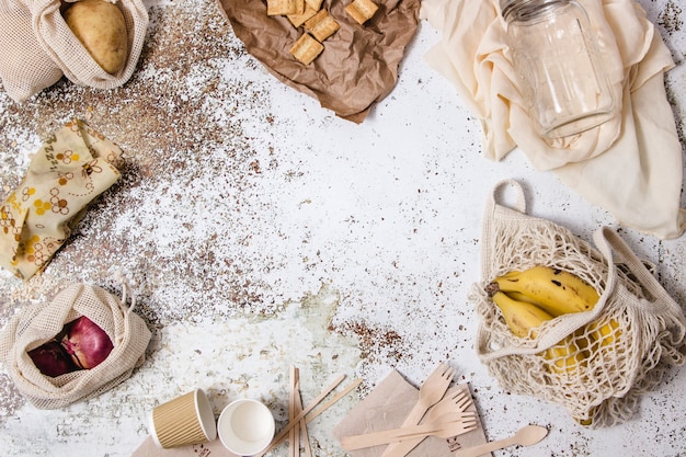 Bowls, dishes, glasses, forks, napkins, different plastic free tableware, shopping bag, glass canister and bees wrap reutilizable displayed around a table with different ingredients, coffe and milk