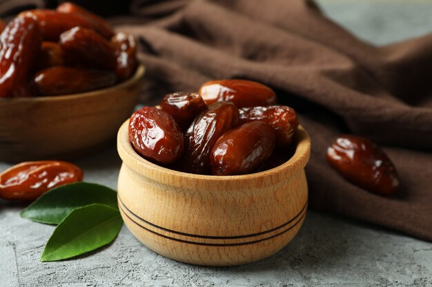 Bowls of dried dates and kitchen napkin on gray textured background