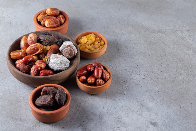 Bowls of dried organic dates, persimmons and raisins on stone surface