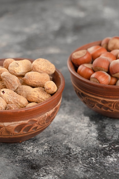 Bowls full of healthy peanuts and hazelnuts in shell placed on a stone table .