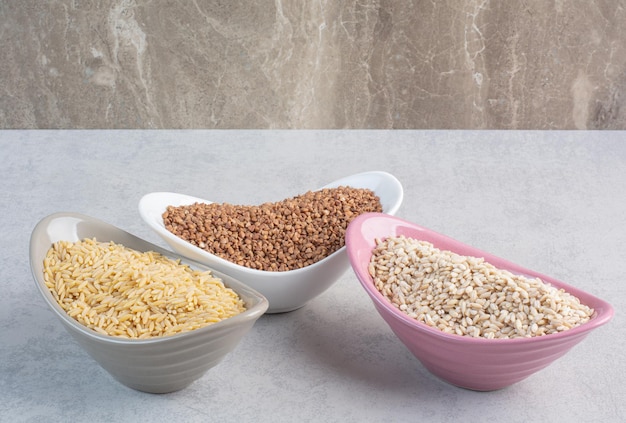 Bowls of rice wheat and buckwheat on marble background