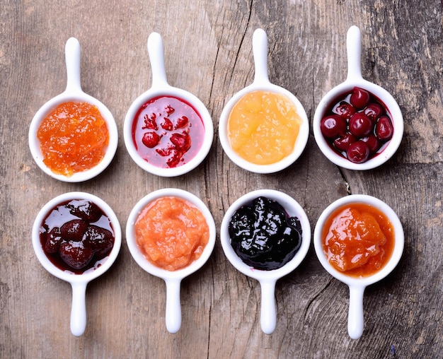 Bowls of tasty jam on wooden background