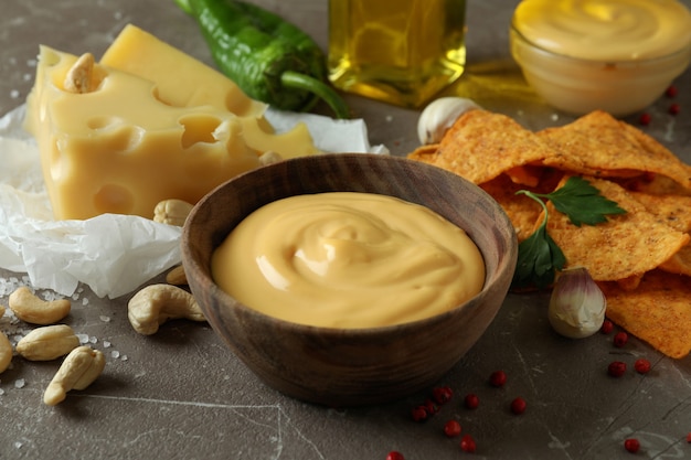 Bowls with cheese sauce and ingredients on gray textured table