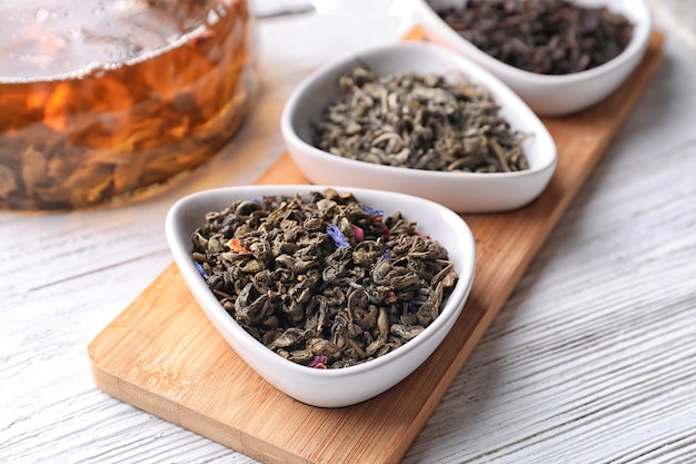 Bowls with different kinds of tea leaves on wooden board