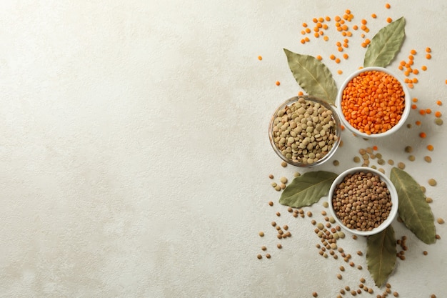 Bowls with different legumes and bay leaves on white surface