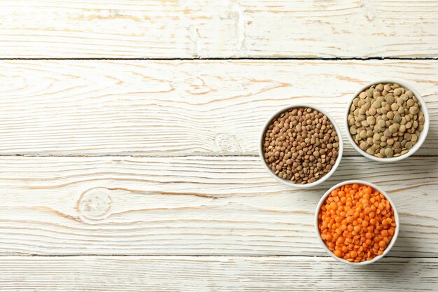 Bowls with different legumes on wooden table, space for text