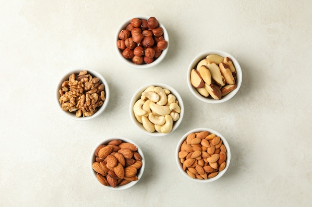 Bowls with different nuts on white textured, top view