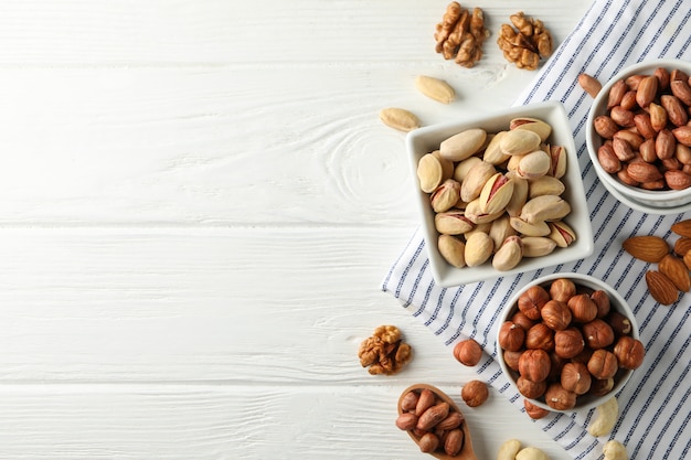 Bowls with different nuts on white wooden background