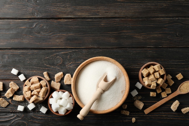 Bowls with different sugar on wooden background, top view