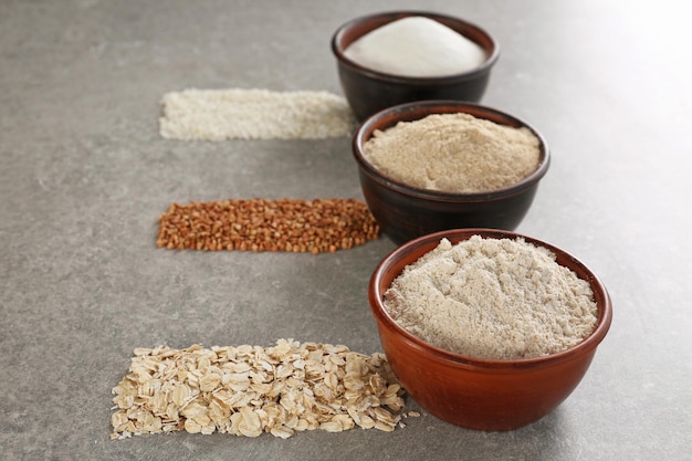 Bowls with different types of flour on gray background