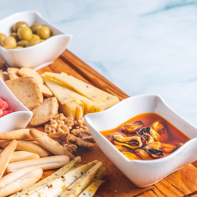 Bowls with picked mussels and olives on a cheese board and breadsticks on a white table