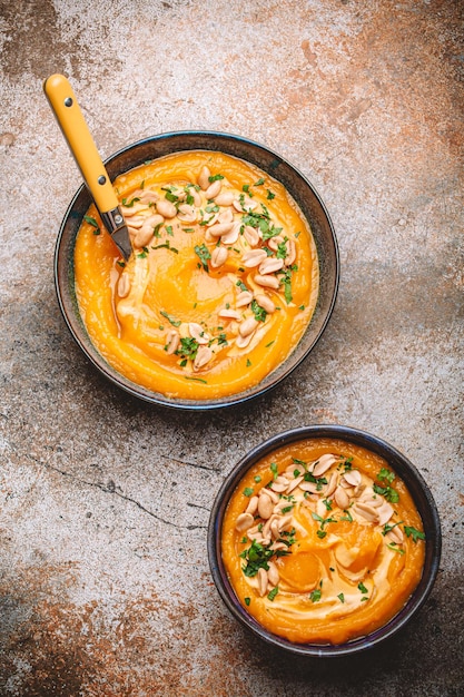 Bowls with pumpkin cream soup with peanuts on rustic metal background