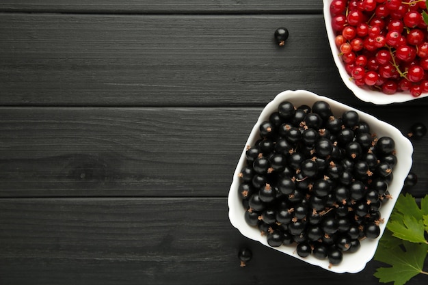 Bowls with ripe red and black currant on black background