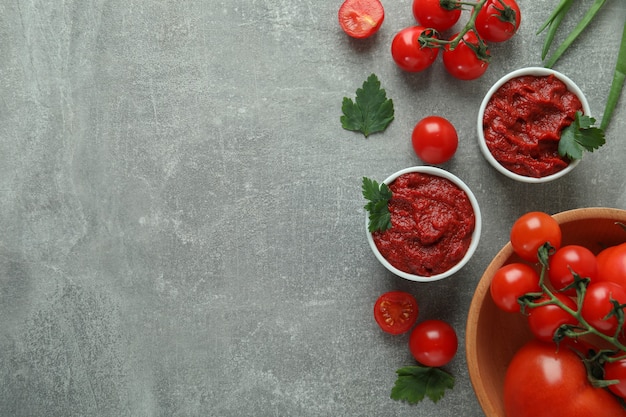 Bowls with tomato paste on gray background with ingredients