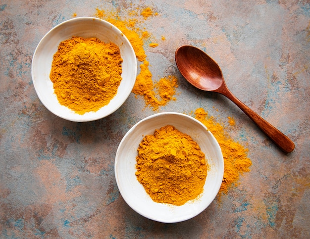 Photo bowls with turmeric powder and wooden spoons on a concrete surface