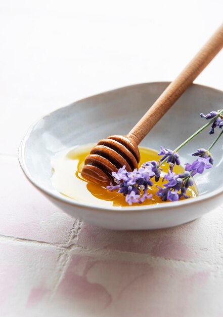 Bowlwith honey and fresh lavender flowers on a pink tile background