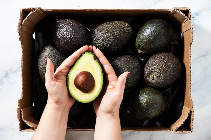 A box of avocado on the table and female hands