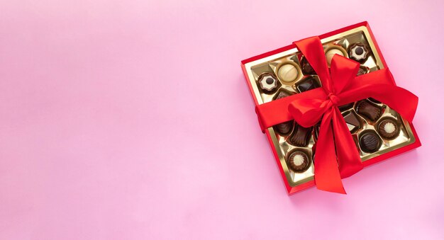 Box of chocolate pralines with red bow on pink