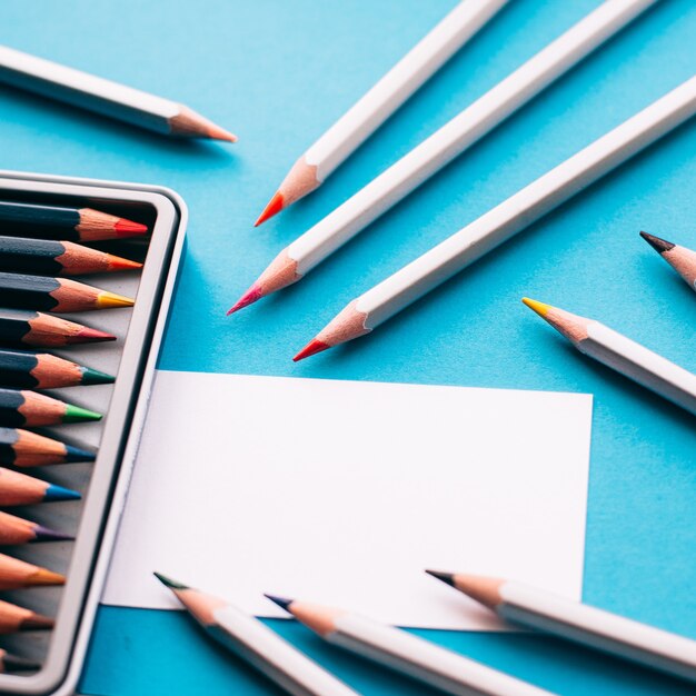 Box of colorful pencils paper sheet on blue