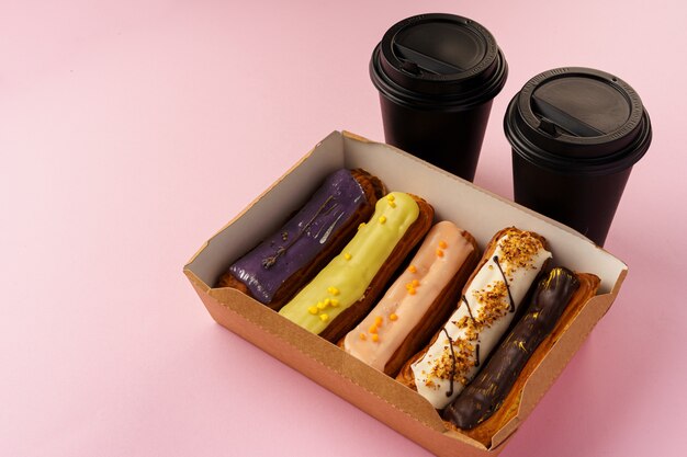 Box of eclairs with takeaway coffee cups on pink background