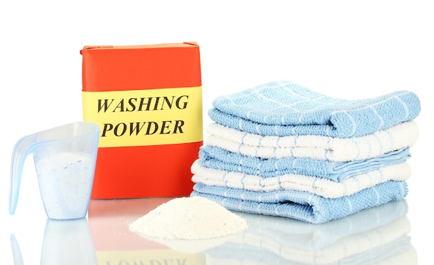 Photo box of washing powder with blue measuring cup and towels isolated on white