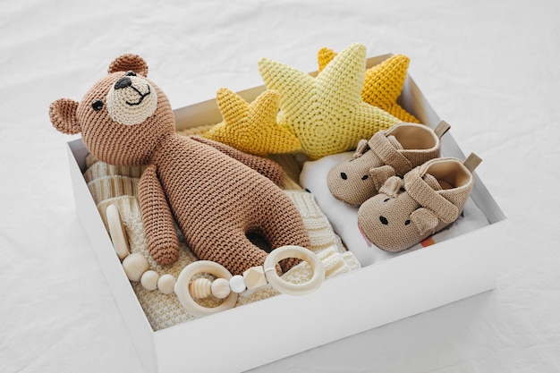 Коробка с детскими вещами и аксессуарами для новорожденных на кровати. Подарочная коробка с вязанным пледом, одеждой, носками, обувью и игрушкой. Концепция детского душа. Плоская планировка, вид сверху
