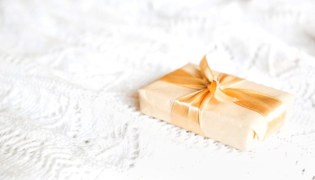 Box with Christmas gift in light paper is tied with a gold ribbon