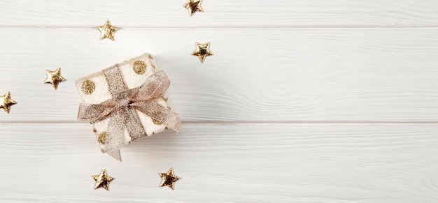 box with a christmas present and gold stars on a white wooden background top view new year banner