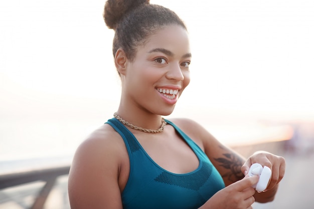 Box with earphones. Beaming woman wearing bright top holding box with earphones while working out outside