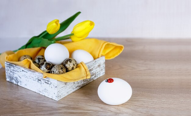 나무 테이블에 부활절 달걀과 노란 튤립이 있는 상자