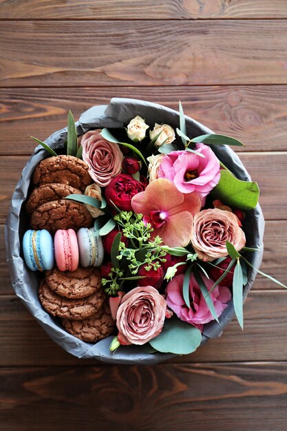 Box with fresh flowers and macaroons on wooden background top view