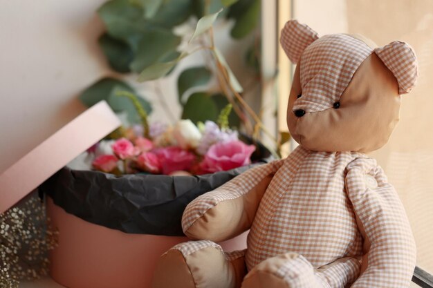 Box with fresh flowers and teddy bear on the windowsill