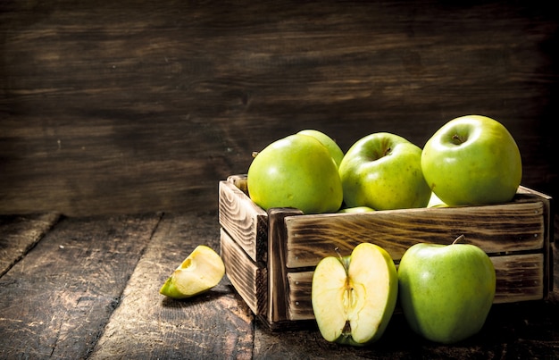 Box with green apples on wooden table.