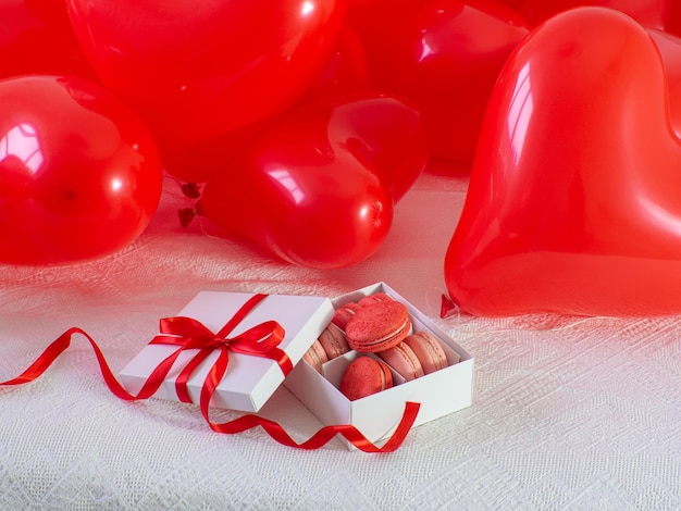 Box with macaron cookies and red baloons on the bed