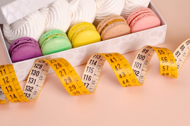 Photo a box with macaroons and meringues and measuring tape on pink