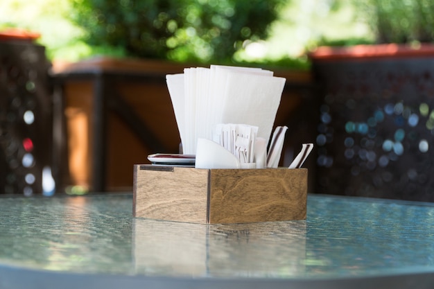 유리 테이블에 종이 냅킨이 있는 상자 클로즈업. 테이블 설정 야외 여름 카페의 일부
