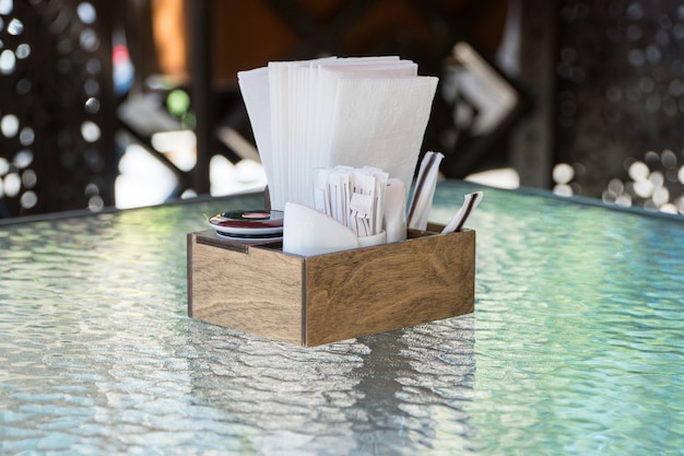 Box with paper napkins on a glass table, close-up. part of the table setting outdoor summer cafe