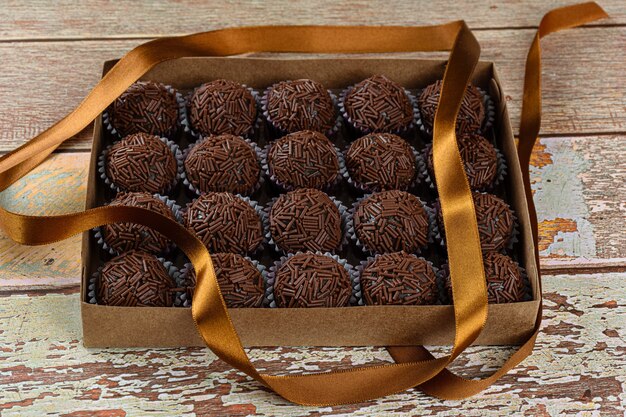 Box with several brigadeiros lined up next to a bow ribbon. Brazilian traditional sweet (side view).