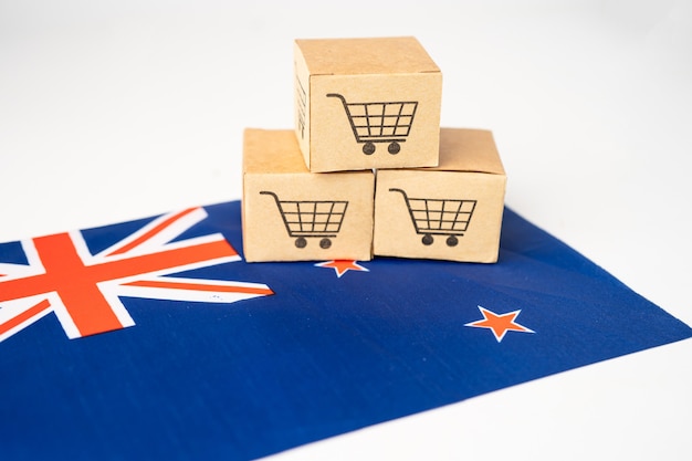 ショッピングカートのロゴとニュージーランドの国旗が付いたボックス、オンラインでの輸出入ショッピング、またはeコマースファイナンスデリバリーサービスストアの製品配送、貿易、サプライヤーのコンセプト。