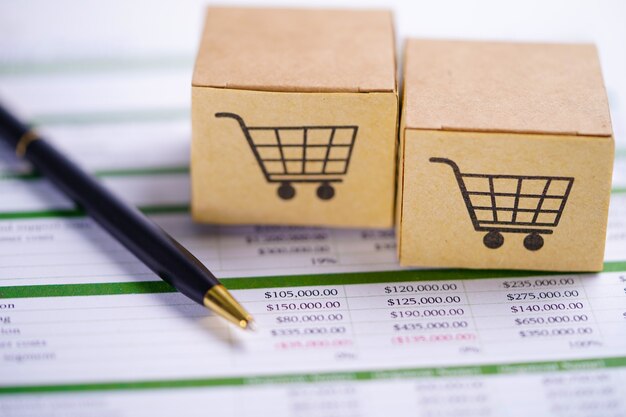 Box with shopping cart logo on spreadsheet paper with pen.