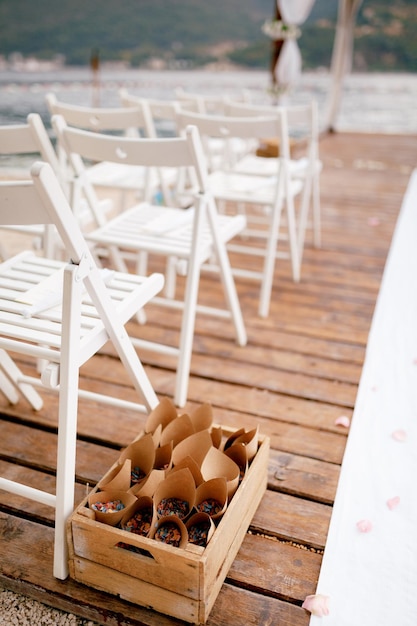 Box with twisted envelopes with flower petals stands next to a row of white chairs