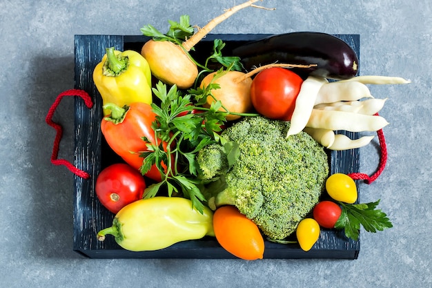 Box with various fresh vegetables on blue textured background  New harvest