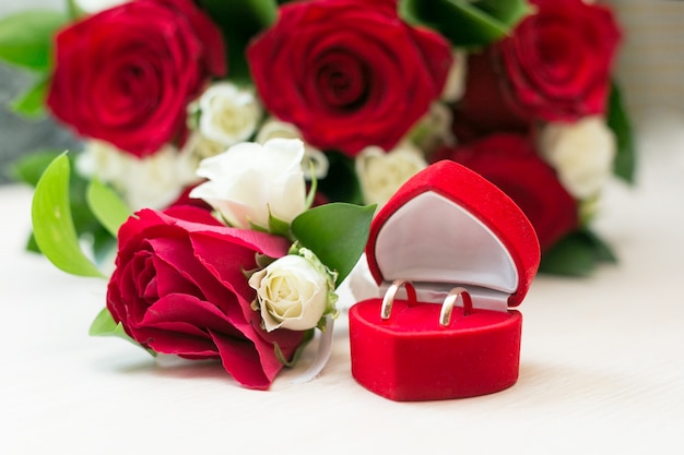 box with wedding rings on a table next to a beautiful bouquet of white and red roses.