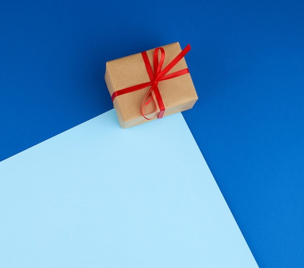 Box wrapped in brown paper and tied with a red bow, gift on blue