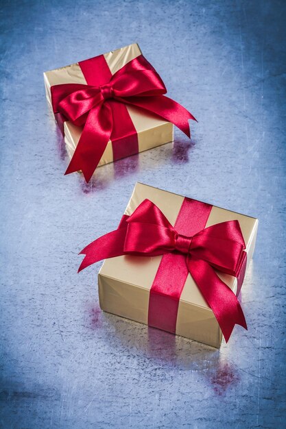 Boxed golden gifts with red bow on scratched metallic background