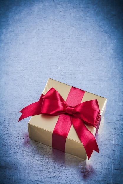 Boxed golden present with red ribbon on metallic background