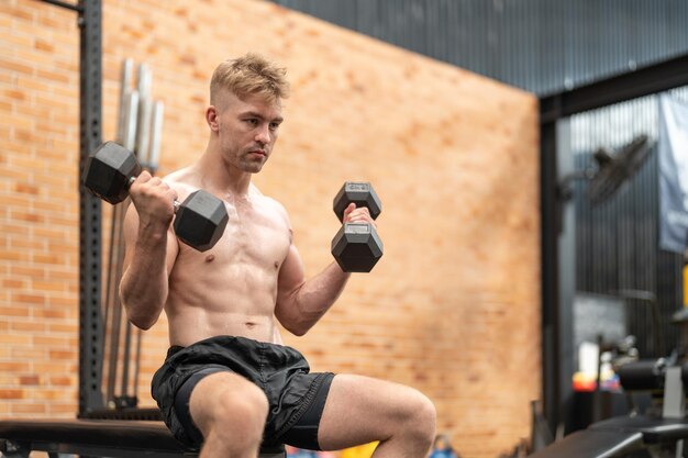 Photo boxer athlete man in shirtless exercising with dumbbell weights at the gym